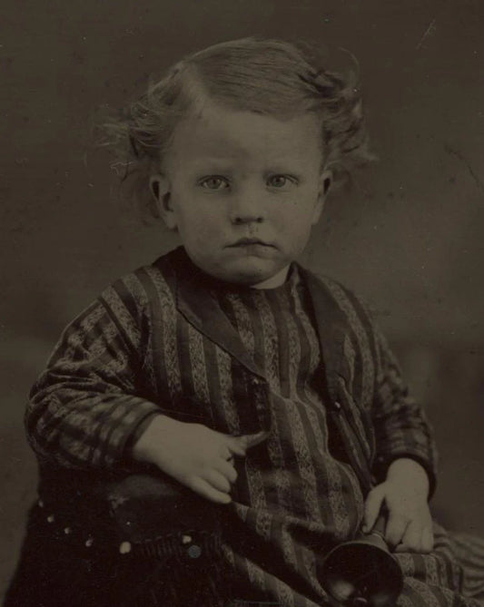 TINTYPE YOUNG CHILD IN STRIPED AND CHECK OUTFIT HOLDING A BELL. TINTED. UNHAPPY.